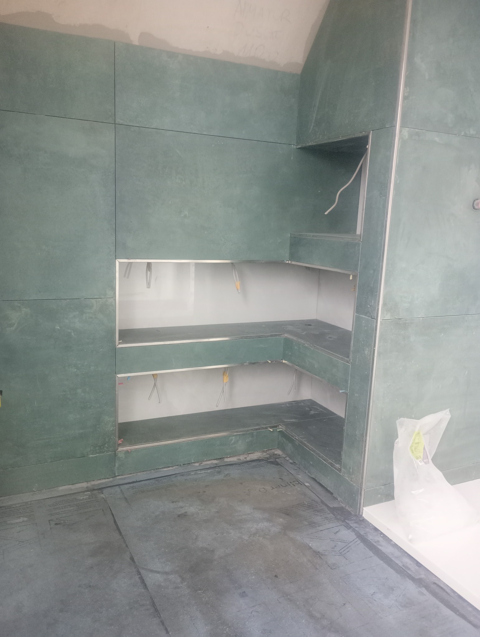 Narożna zabudowa z płyt GK w surowym stanie, z widocznymi przewodami elektrycznymi. Szare płyty na ścianach i podłodze, białe wnętrze wnęk.