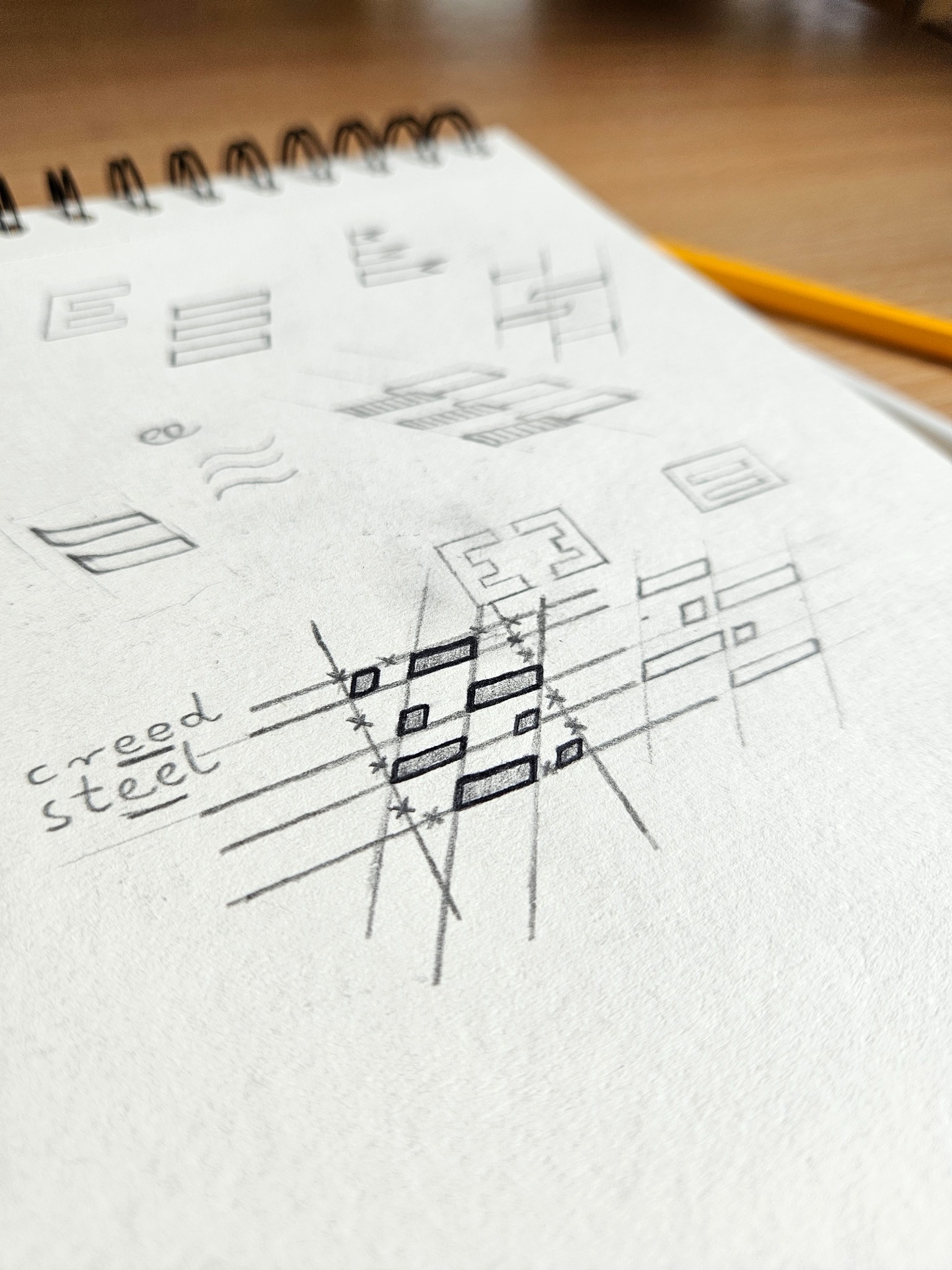 Szkicownik z koncepcjami logo 'Creed Steel' w Kolbudach. Ręcznie rysowane projekty, w tym jeden z zaznaczonymi proporcjami i liniami pomocniczymi.