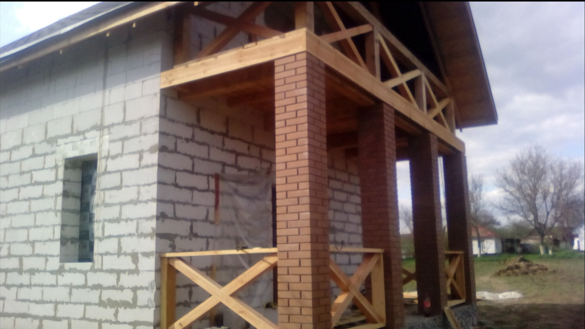 Budynek w trakcie budowy z białego bloczka, z elementami z cegły i drewnianą konstrukcją dachu. Widoczne rusztowania i niezabudowane otwory okienne.