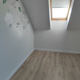 Home-Bud Grzegorz Musz - Jasne panele podłogowe w pokoju na poddaszu z oknem dachowym i ścianą ozdobioną delikatnymi, kwiatowymi naklejkami. Minimalistyczne wykończenie wnętrza.