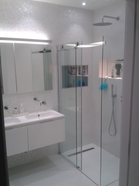 Nowoczesna, biała łazienka z kabiną prysznicową typu walk-in, podwójną umywalką i lustrem z oświetleniem LED. Minimalistyczny design, błyszczące płytki na ścianach.