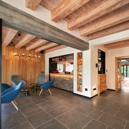 Łukasz Wykończenia - Nowoczesne wykończenie wnętrza hotelu z drewnianym sufitem, stylowymi krzesłami i widokiem na zieleń. Charakterystyczne oświetlenie i kamienna okładzina baru.