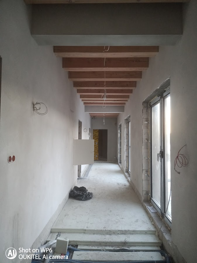 Korytarz w trakcie prac wykończeniowych w Hotelu Siedlisko Milachowo: surowe ściany, drewniane belki sufitowe, okna bez wykończenia, instalacje elektryczne.