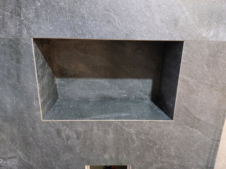 Wnęka wykończona szarą, kamienną okładziną, z widocznymi fugami. Minimalistyczny design w łazience, podkreślony przez precyzyjne ułożenie płytek i subtelne oświetlenie.