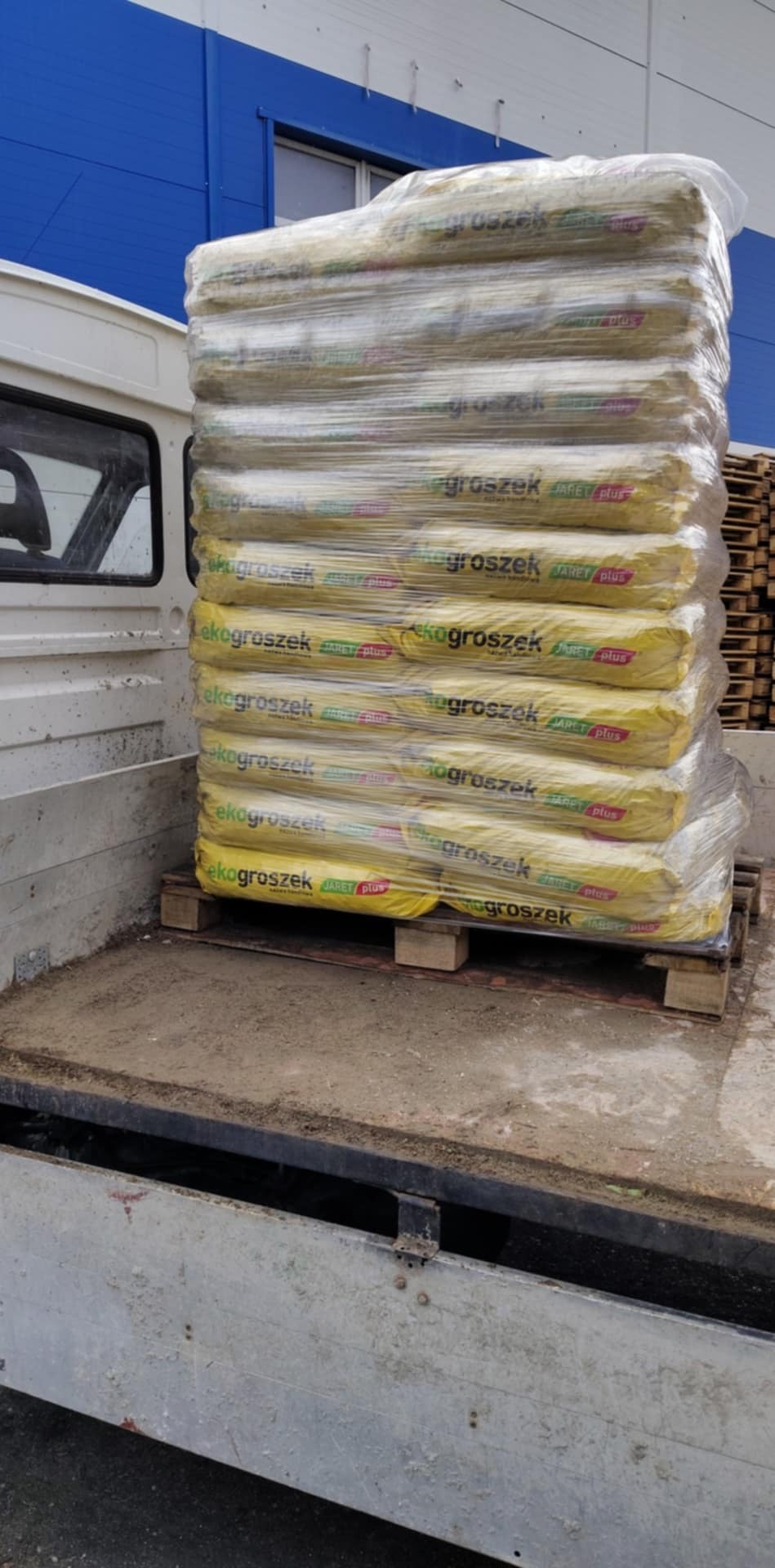 Załadunek worków ekogroszku na palecie w przestrzeni ładunkowej samochodu dostawczego, widok z boku, opakowania zafoliowane.