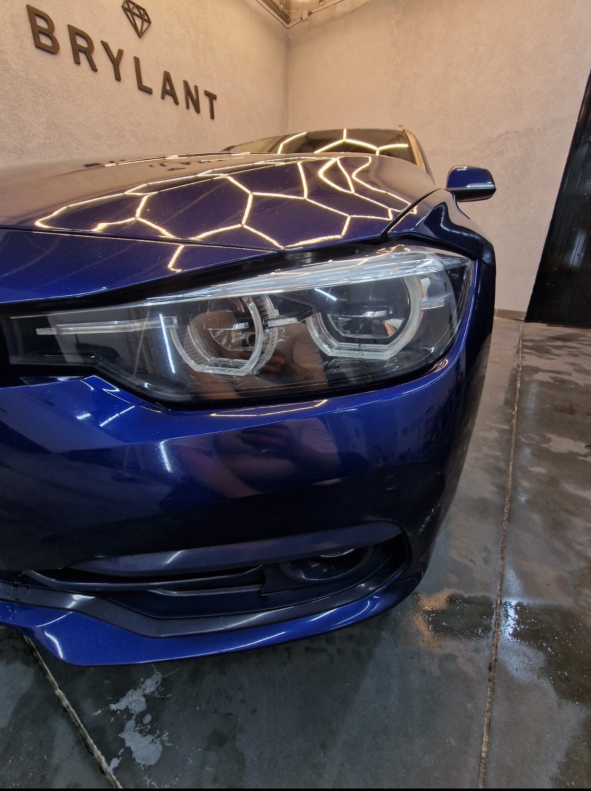 Błyszczący, granatowy samochód marki BMW po detailingu, z widocznymi refleksami świetlnymi na karoserii. W tle logo firmy 'BRYLANT'.