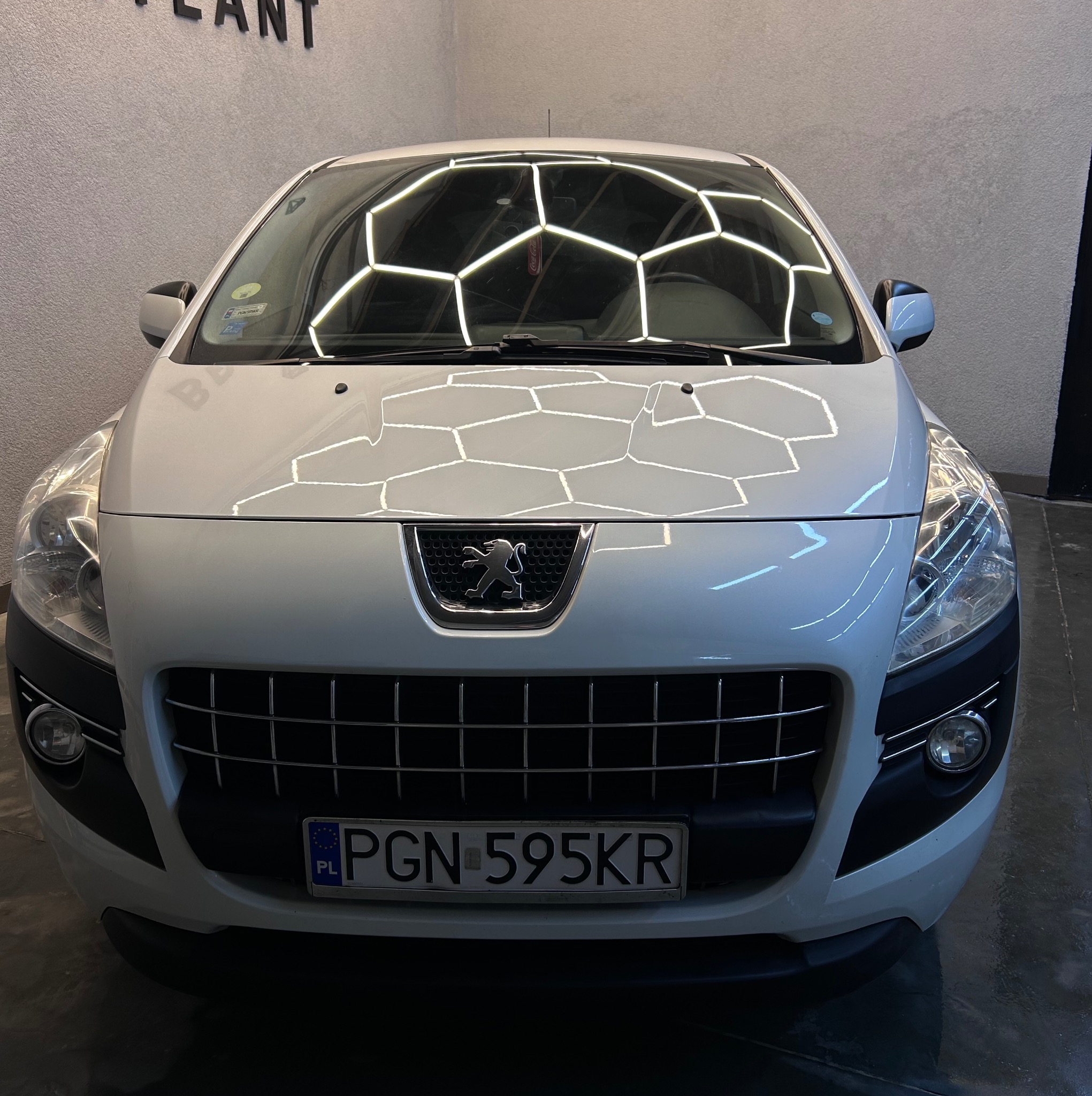 Biały Peugeot 3008 po umyciu w myjni, widok z przodu, z odbiciami heksagonalnych świateł na karoserii. Widoczna tablica rejestracyjna PGN 595KR.