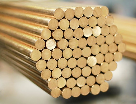 Zestaw gładkich, miedzianych prętów o okrągłym przekroju, ułożonych równolegle w zwartym pakiecie. Metal o ciepłym odcieniu, widoczne refleksy światła.