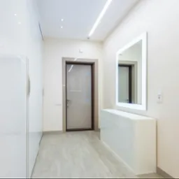 Jasny przedpokój z oświetleniem LED: listwa na suficie, podświetlane lustro. Minimalistyczny design, białe meble z połyskiem, szara stolarka drzwiowa.