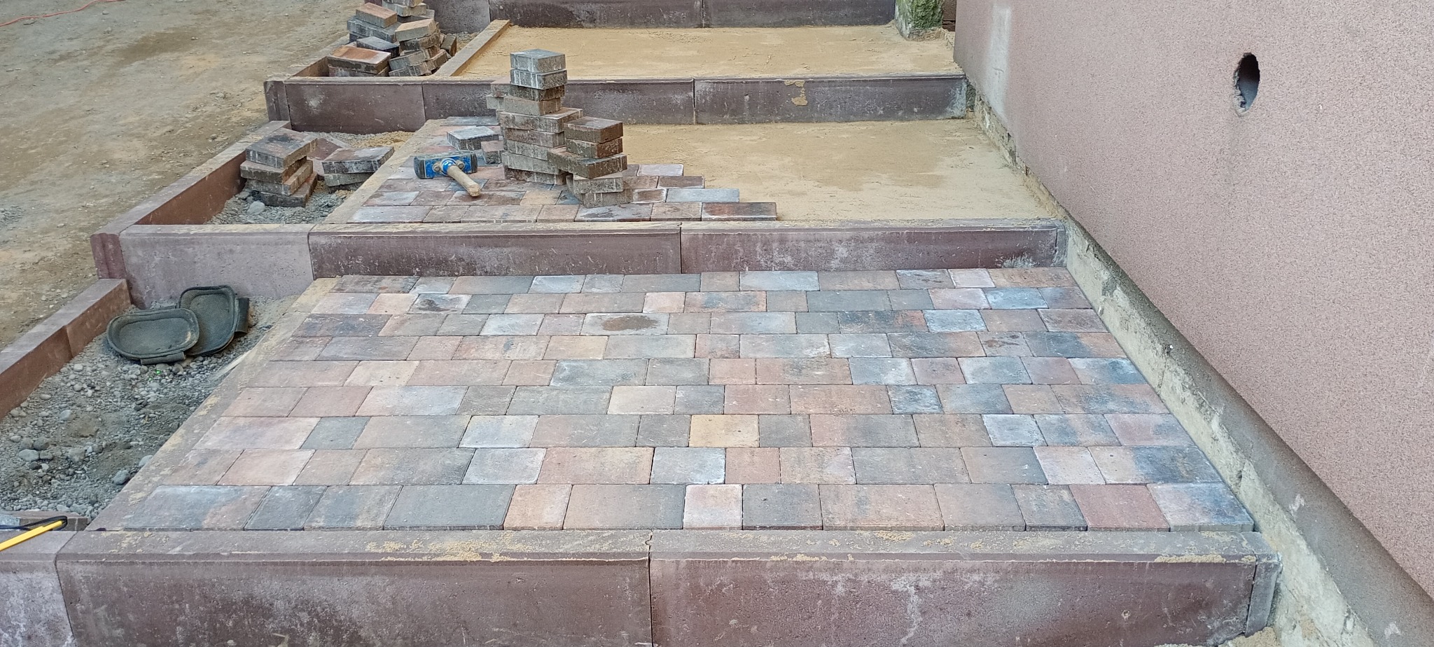 Etap prac brukarskich w Poznaniu: częściowo ułożona kostka brukowa w odcieniach szarości i brązu, widoczne narzędzia, klepisko i przygotowane materiały.