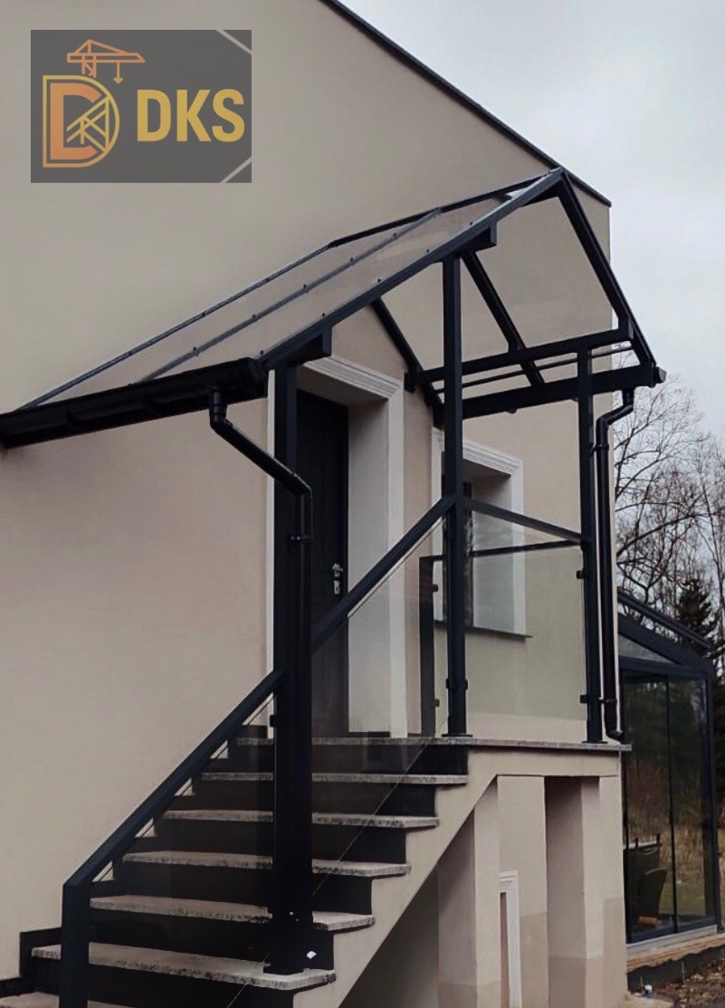 Zadaszenie nad schodami wejściowymi z czarną, metalową konstrukcją i przezroczystym wypełnieniem. Dodatkowo balustrady ze szkła i metalu. Widok z dołu.