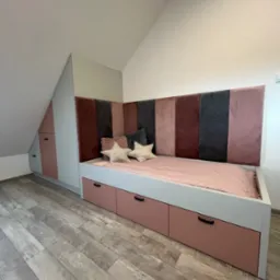 Pokój dziecięcy na poddaszu: zabudowa szafy wnękowej z łóżkiem z szufladami, tapicerowany zagłówek w odcieniach różu i szarości, poduszki w kształcie gwiazd.