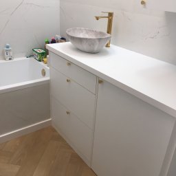 Peleda - Nowoczesna łazienka z białą szafką na wymiar, marmurową umywalką i złotą armaturą. Parkiet w jodełkę. Minimalistyczny design z akcentami luksusu.