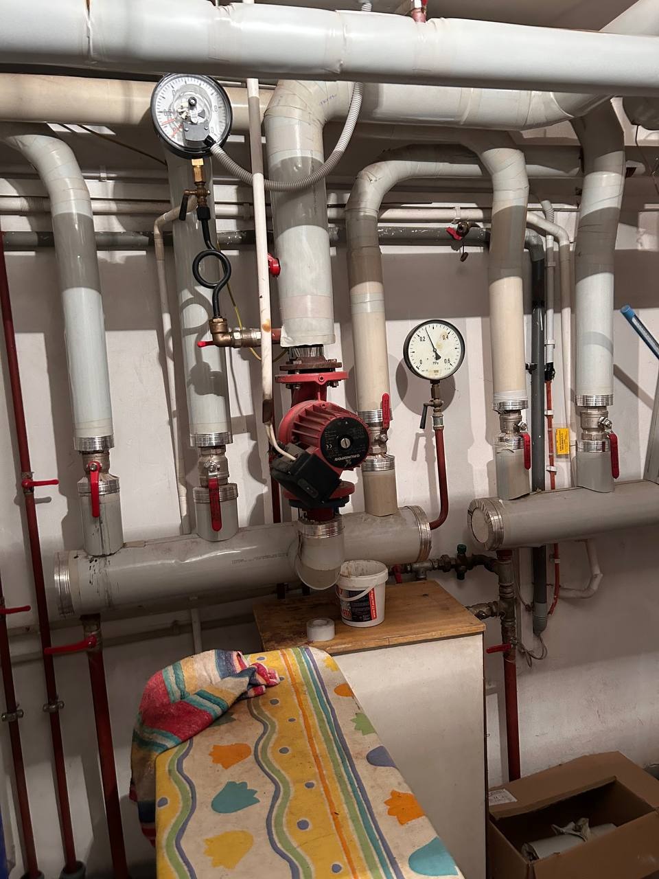 Kompleksowy system rur centralnego ogrzewania z manometrami i pompą obiegową, widoczne elementy instalacji grzewczej w piwnicy, osprzęt i narzędzia.