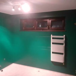 Marcin Tokarski - Wykończona łazienka z zielonymi ścianami, brązowym oknem i białym grzejnikiem drabinkowym. Widoczne punkty świetlne na suficie i biała podłoga.