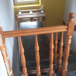 Marcin Tokarski - Malowanie klatki schodowej: pomalowane ściany na żółto, drewniana balustrada w trakcie malowania, zabezpieczona podłoga folią malarską. Widok z góry.