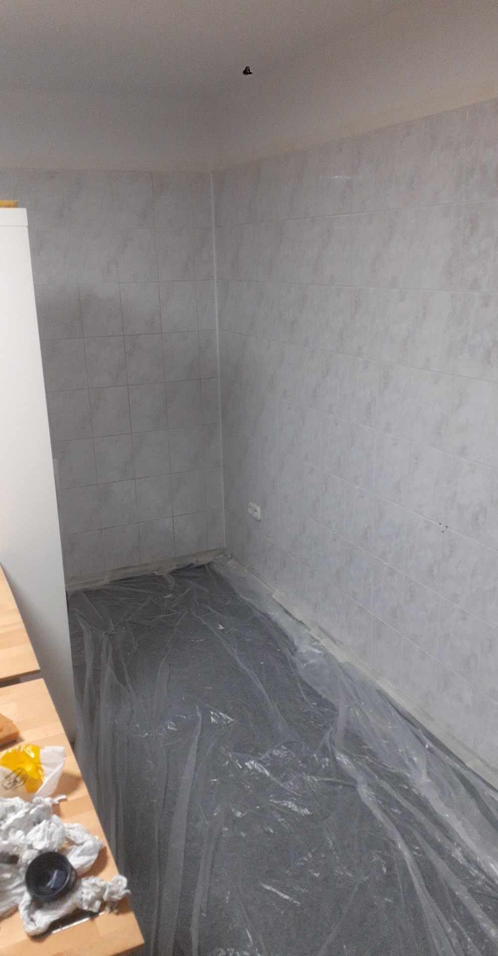 Przygotowanie do prac wykończeniowych: podłoga zabezpieczona folią malarską w pomieszczeniu z wyłożonymi płytkami ścianami. Widoczne akcesoria malarskie.