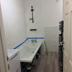 ELWENT DAWID KLIM - Biała łazienka z marmurowymi płytkami, nową wanną zabezpieczoną folią, grzejnikiem drabinkowym i szafką pod umywalkę, w trakcie lub tuż po remoncie.