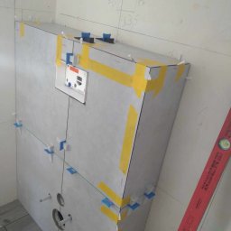 ELWENT DAWID KLIM - W trakcie prac glazurniczych w Białymstoku: montaż stelaża podtynkowego z obudową z płytek. Widoczne poziomica, taśma malarska i system poziomowania płytek.