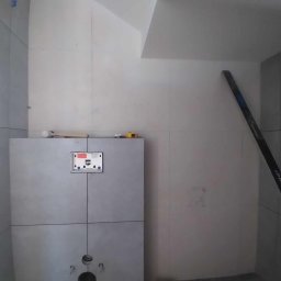 ELWENT DAWID KLIM - Szare płytki w łazience, widoczny stelaż podtynkowy WC, poziomica oparta o ścianę. Minimalistyczne wykończenie, surowy styl.