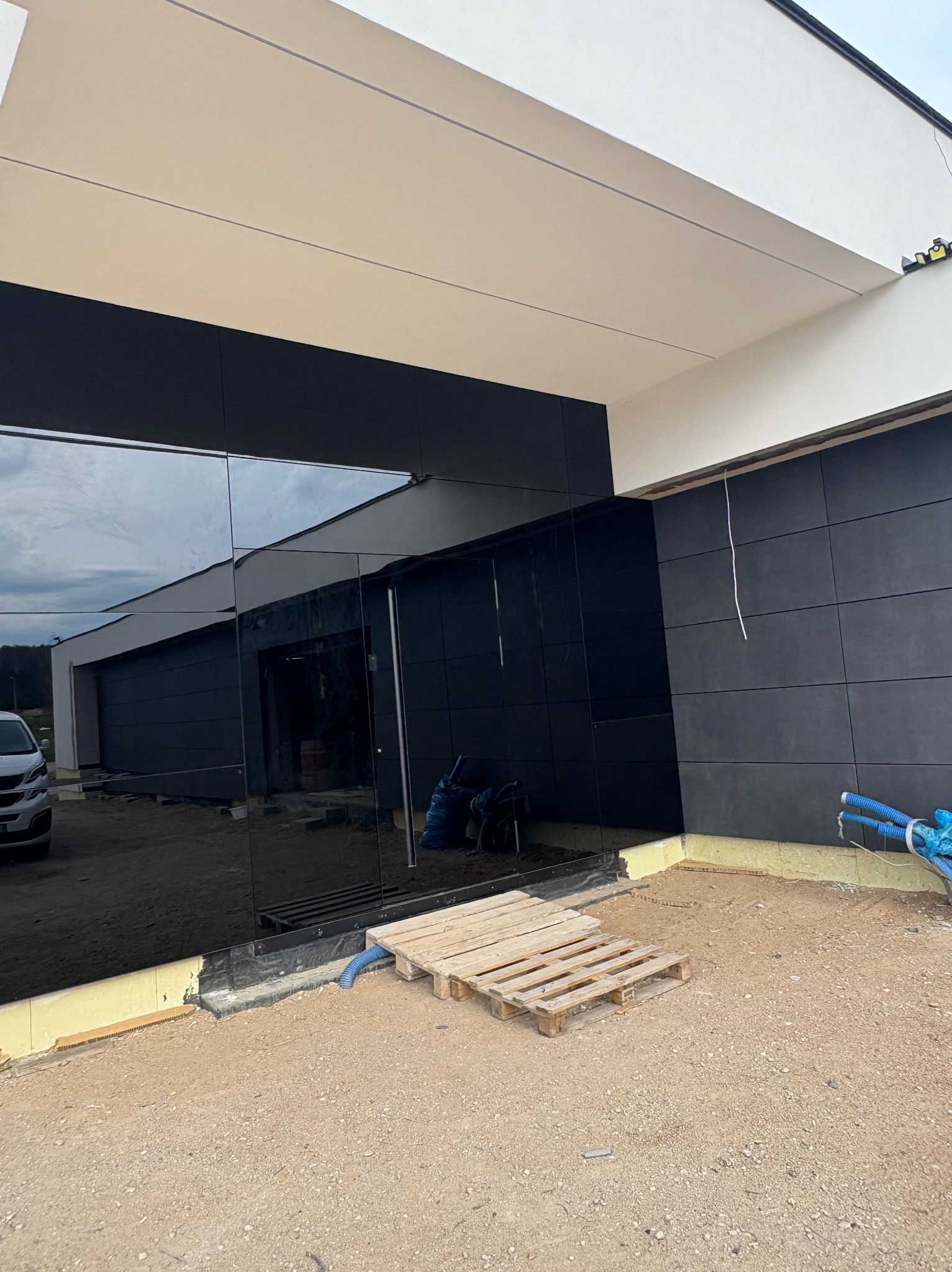 Elewacja budynku z czarnymi płytami i lustrzanymi panelami. Widoczne materiały budowlane i instalacje. Ujęcie z dołu, akcent na detale wykończeniowe.