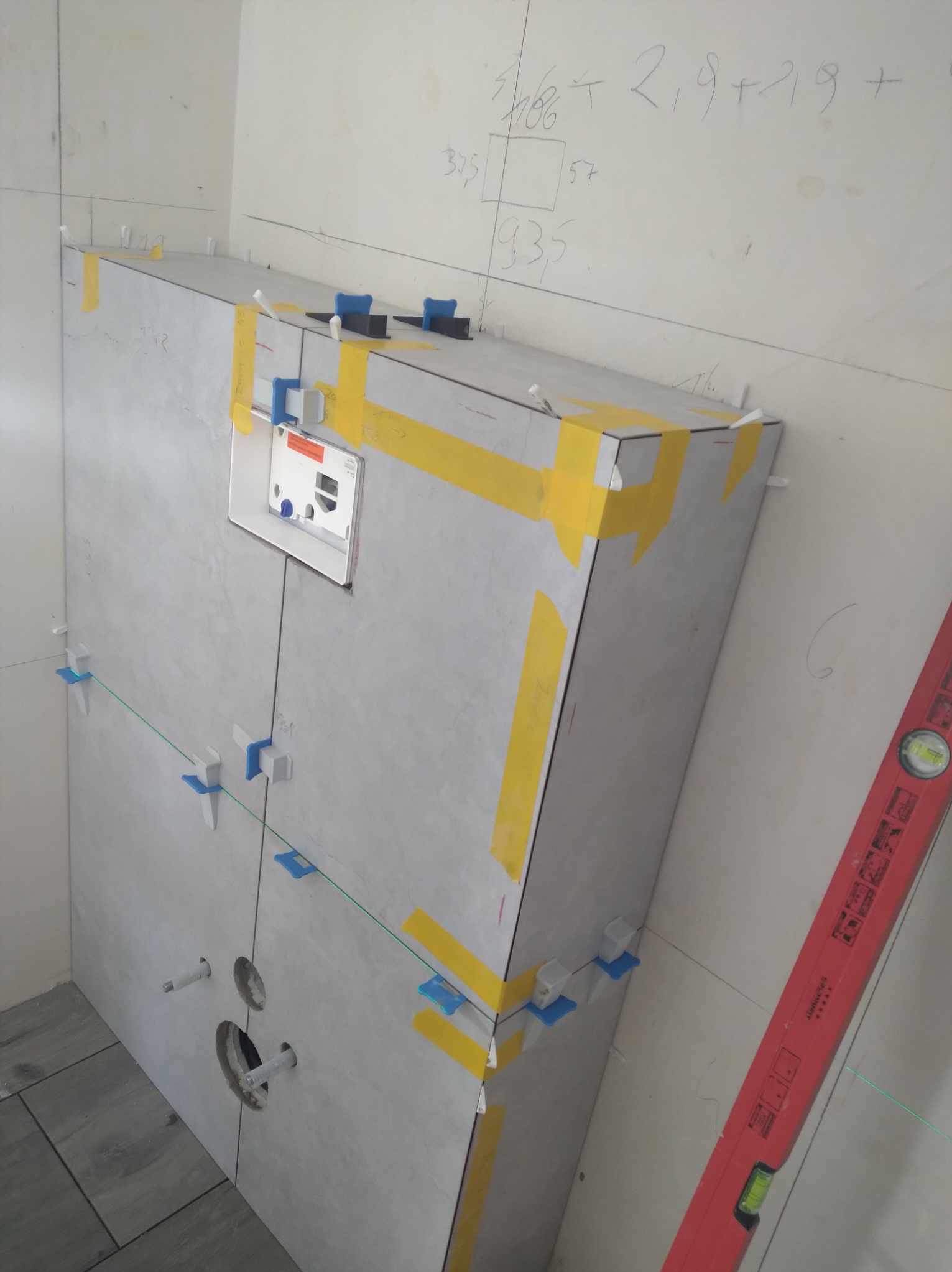 W trakcie prac glazurniczych w Białymstoku: montaż stelaża podtynkowego z obudową z płytek. Widoczne poziomica, taśma malarska i system poziomowania płytek.