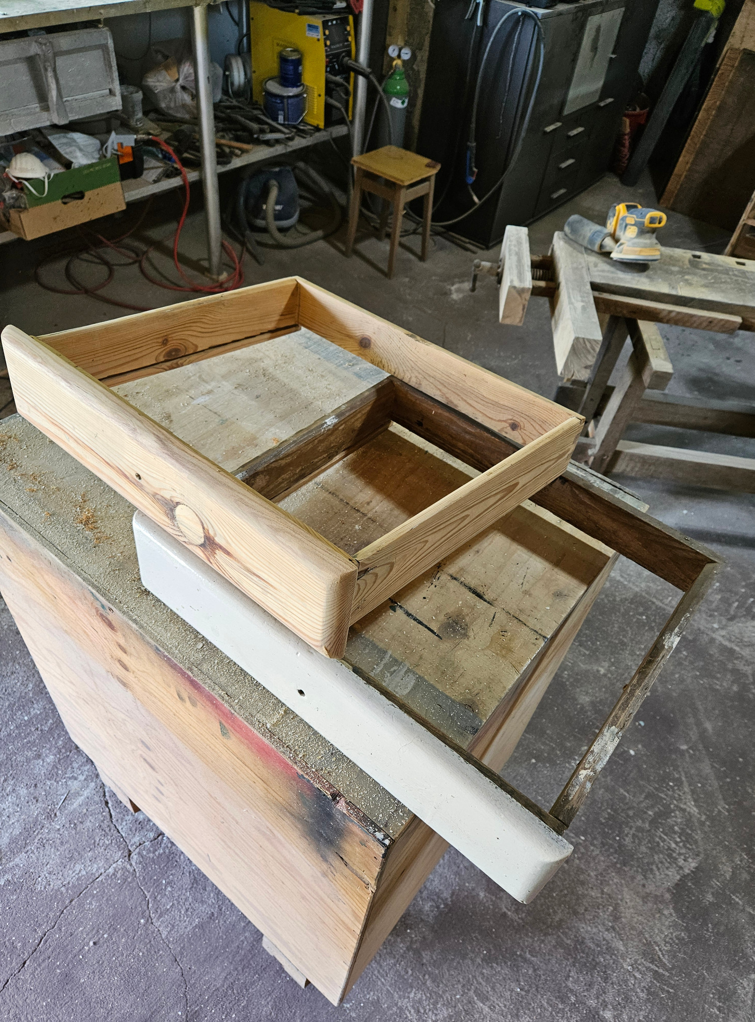 Drewniana rama szuflady w warsztacie stolarskim, widoczne ślady obróbki drewna i narzędzia w tle. Jasne drewno, surowy charakter, realistyczne ujęcie.