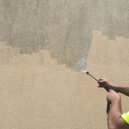 BRUKCLEAN Damian Rzodkiewicz - Czyszczenie elewacji beżowej ściany z fakturą za pomocą myjki ciśnieniowej. Widoczna różnica w kolorze przed i po czyszczeniu.