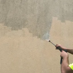 Czyszczenie elewacji beżowej ściany z fakturą za pomocą myjki ciśnieniowej. Widoczna różnica w kolorze przed i po czyszczeniu.