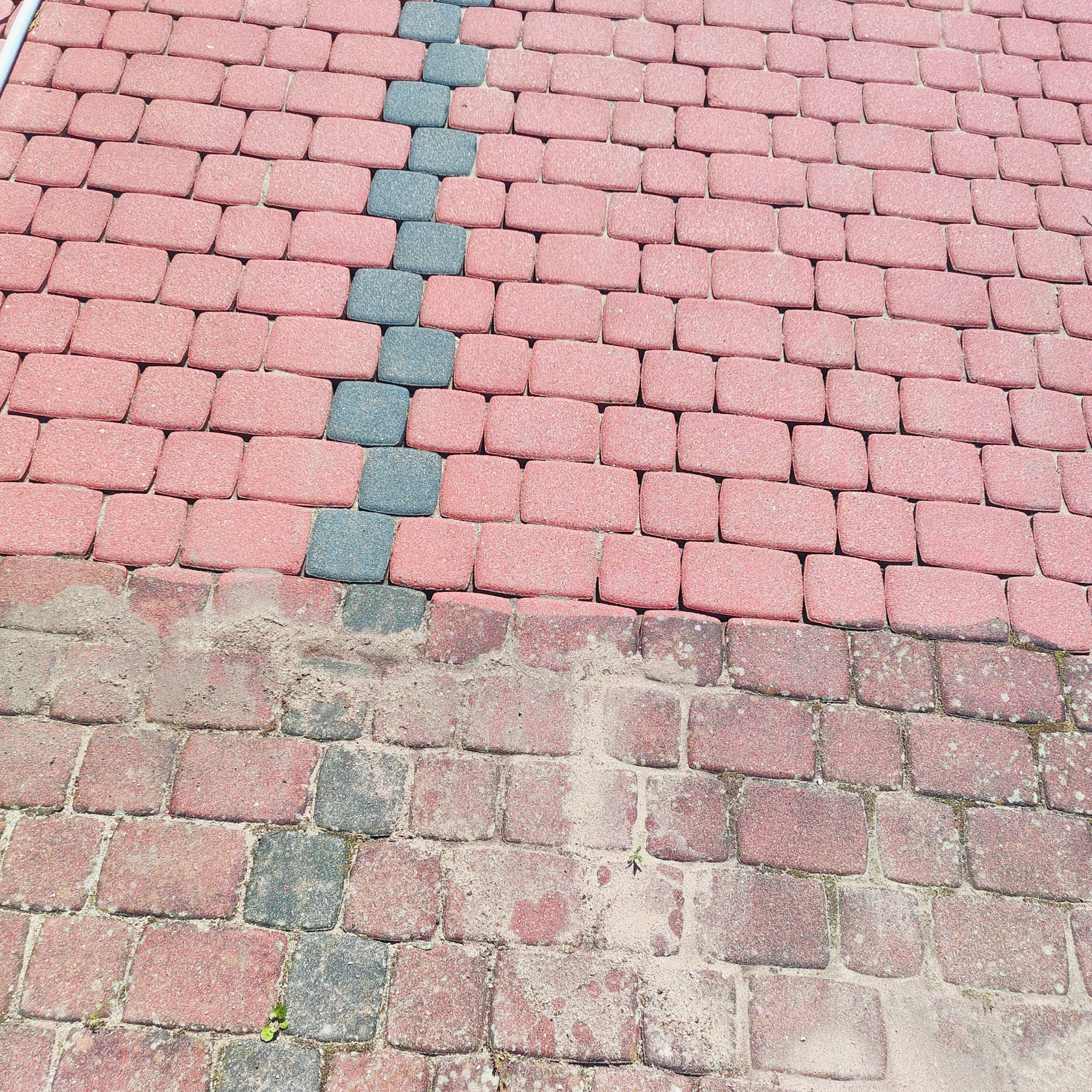 Fragment kostki brukowej z różową i szarą kostką, widoczna różnica w czystości między górną a dolną częścią kadru. Zdjęcie z bliska, z góry.