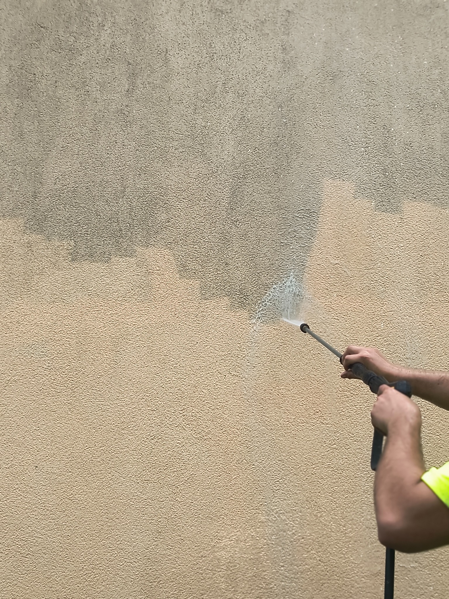Czyszczenie elewacji beżowej ściany z fakturą za pomocą myjki ciśnieniowej. Widoczna różnica w kolorze przed i po czyszczeniu.