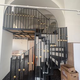 Błażej Cebula Spawart - Spiralne schody metalowe z czarną konstrukcją i złotymi zdobieniami w Popowicach. Widok z dołu, ukazujący detale balustrady i ażurową konstrukcję schodów.