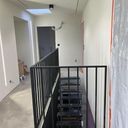 Błażej Cebula Spawart - Nowoczesne schody metalowe z czarną balustradą w surowym wnętrzu. Widoczne przygotowania do dalszych prac wykończeniowych, zabezpieczone ściany folią malarską.