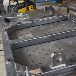 Błażej Cebula Spawart - Metalowa konstrukcja spawana na perforowanym stole warsztatowym, widoczne spoiny i uchwyty montażowe. W tle spawarka ESAB.