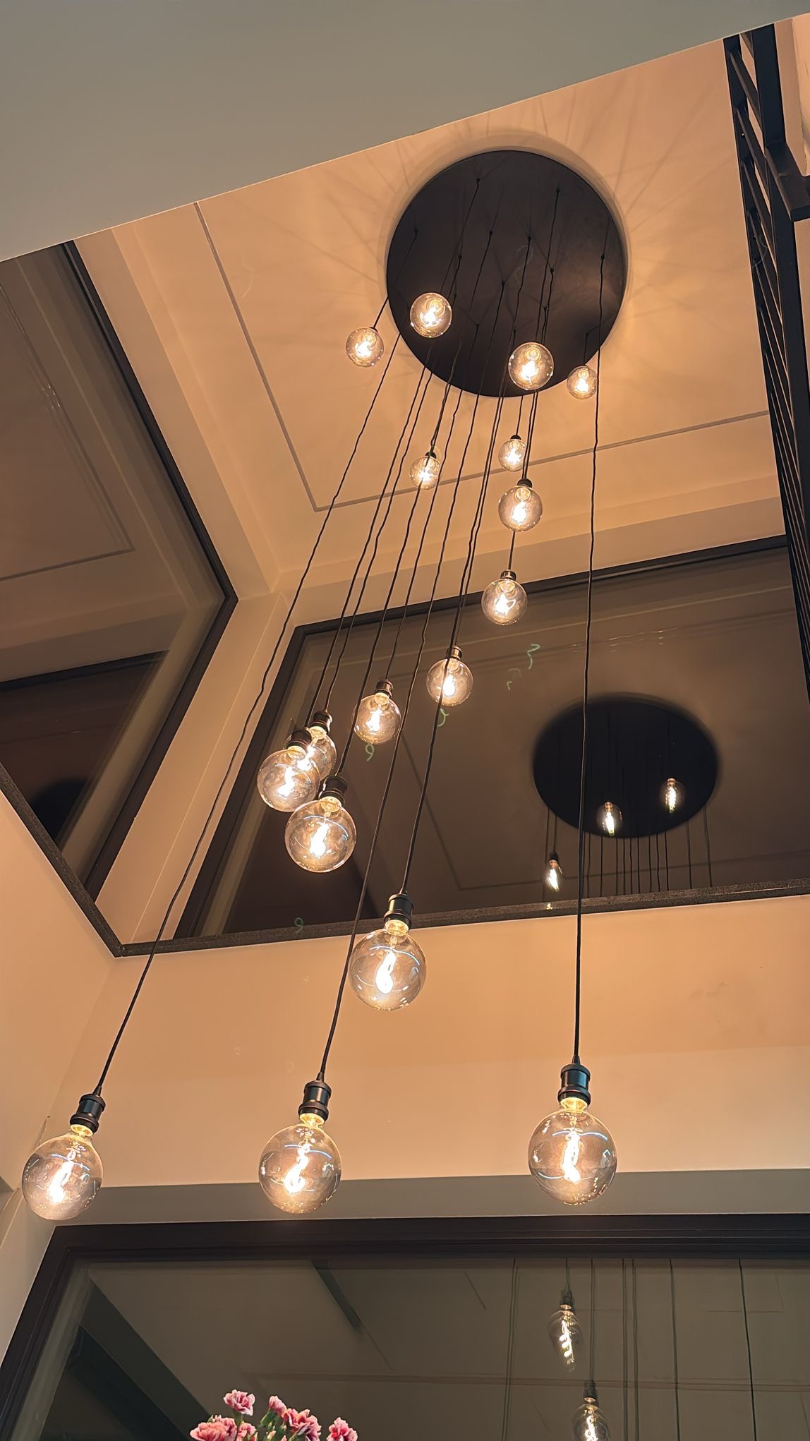 Nowoczesna lampa wisząca z wieloma żarówkami w kształcie kul, zawieszonymi na różnych wysokościach, tworząca unikalny efekt świetlny w jasnym wnętrzu.