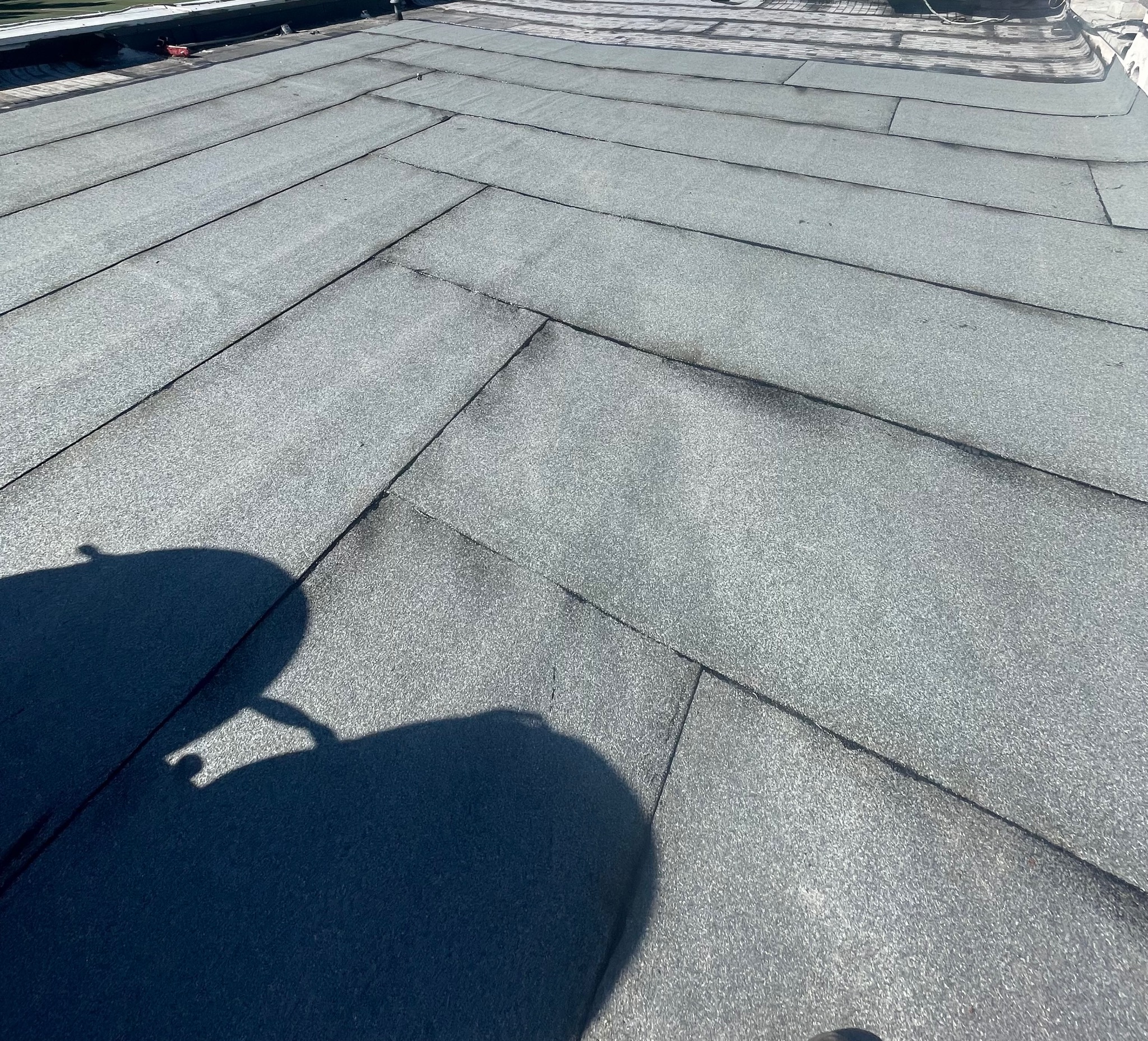Szary, płaski dach pokryty papą bitumiczną ułożoną w jodełkę. Widoczny cień osoby robiącej zdjęcie. Detal pokrycia dachowego.