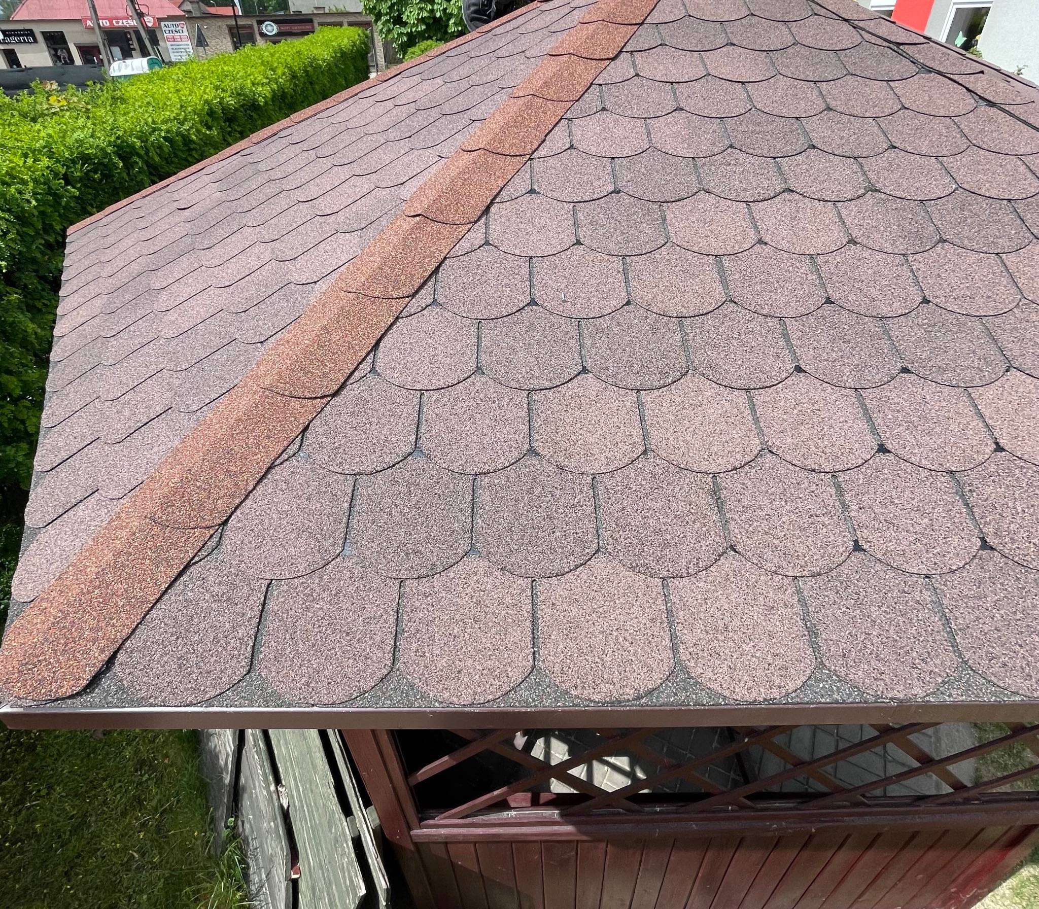 Dach altany pokryty brązowym gontem bitumicznym o wzorze karpiówki, z widoczną listwą kalenicową i elementami konstrukcji altany w tle.