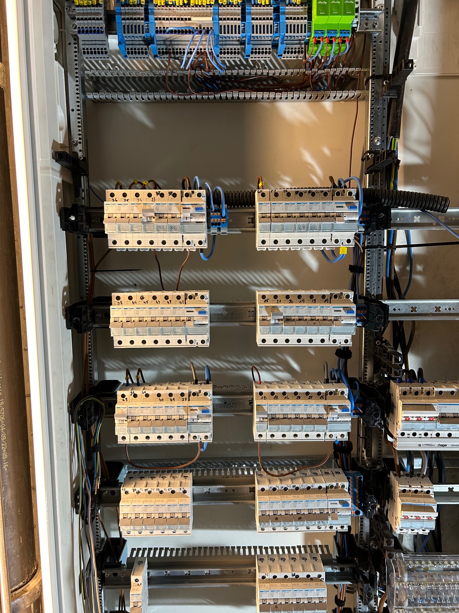 Wnętrze szafy elektrycznej z zamontowanymi bezpiecznikami Hager, złączkami LSA i modułami Shelly, widoczne przewody. Instalacja 'SmartDom'.