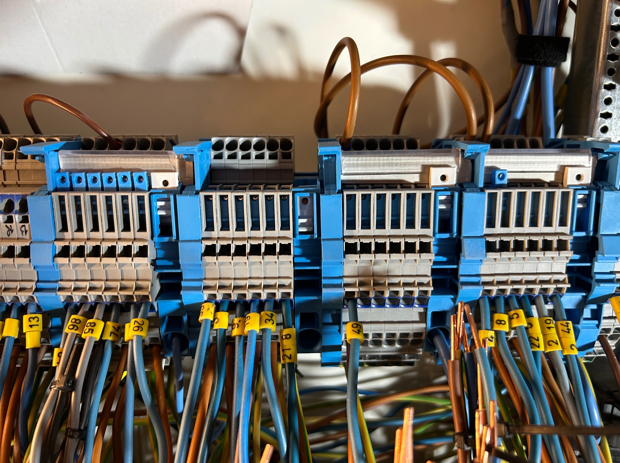 Szczegółowe ujęcie rozdzielnicy elektrycznej z oznaczonymi przewodami, widoczne niebieskie i szare elementy złączek. Przewody w różnych kolorach z żółtymi oznaczeniami.