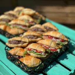 Kruche rogaliki z różnymi nadzieniami, ułożone w koszykach na turkusowym, drewnianym stole w słoneczny dzień. Catering na imprezę firmową.