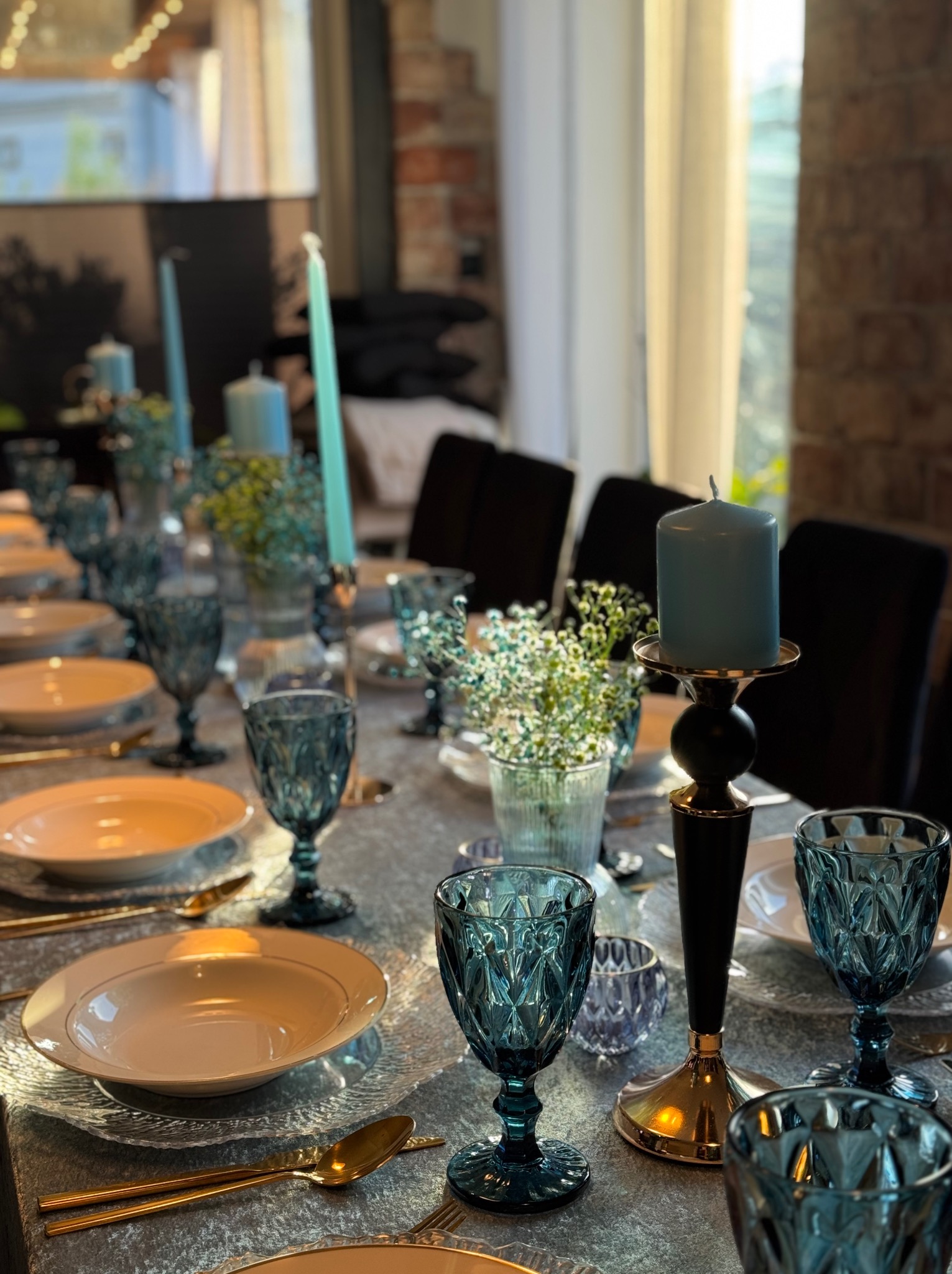 Elegancko nakryty stół z błękitnymi akcentami: świece, kieliszki i kwiaty. Zastawa w odcieniach złota. Idealne na uroczysty catering świąteczny lub firmowy.