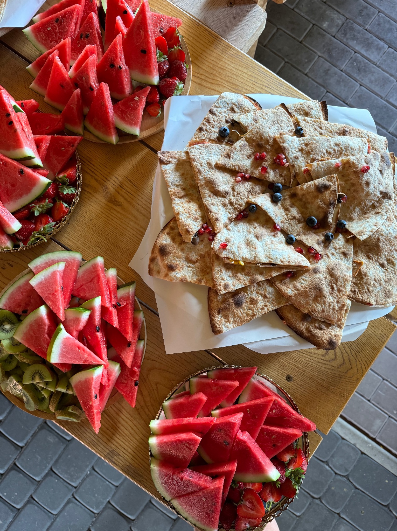 Letni bufet w Damnicy: talerze z truskawkami, arbuzem, kiwi i pitą z owocami na drewnianym stole. Idealne na catering firmowy.