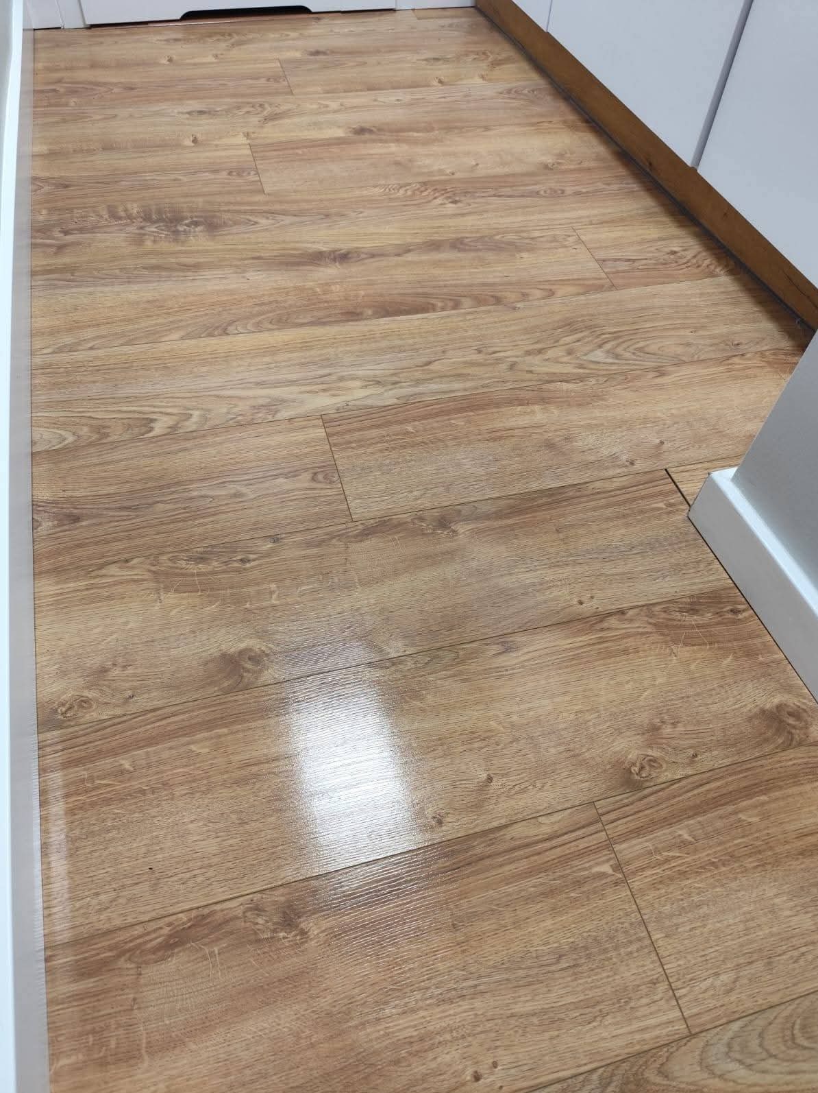 Położona podłoga z paneli drewnopodobnych w Luboniu. Widoczny fragment białej listwy przypodłogowej i szafki. Panele ułożone równolegle do ściany.