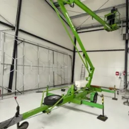 Zielony podnośnik koszowy Niftylift 120 w hali z pracownikiem w koszu, przygotowany do mycia elewacji lub dachu. Widoczna konstrukcja ściany.