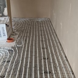 Oleksii Tkachov - Białe rury ogrzewania podłogowego ułożone na siatce, widoczne pudełka z armaturą sanitarną. Etap instalacji w surowym wnętrzu.