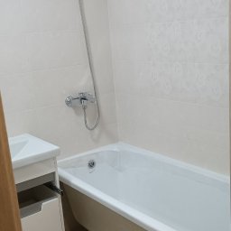 Oleksii Tkachov - Jasna łazienka po remoncie: biała wanna na metalowych nóżkach, umywalka z szafką, błyszczące płytki na ścianach i chromowana armatura.