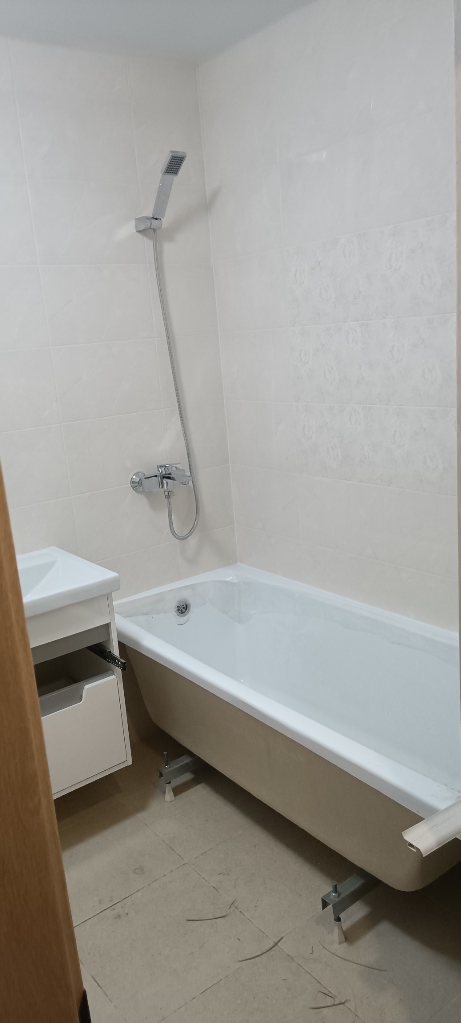 Jasna łazienka po remoncie: biała wanna na metalowych nóżkach, umywalka z szafką, błyszczące płytki na ścianach i chromowana armatura.