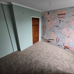 DOKŁADNI.PL SPÓŁKA Z OGRANICZONĄ ODPOWIEDZIALNOŚCIĄ - Pokój dziecięcy po remoncie: ściany pomalowane na zielono, jedna ze ścian z tapetą w mapę świata z motywami podróżniczymi. Ciemny dywan na podłodze i drewniane drzwi.
