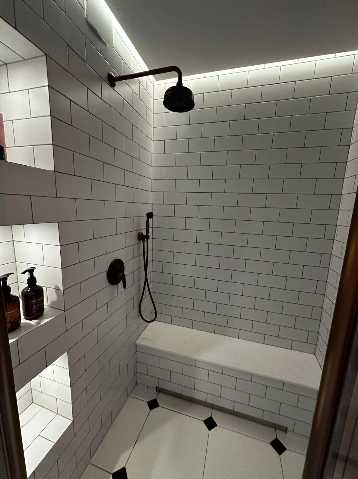 Nowoczesny prysznic z białymi płytkami, czarną armaturą i wnękami na kosmetyki. Subtelne oświetlenie LED podkreśla minimalistyczny design.