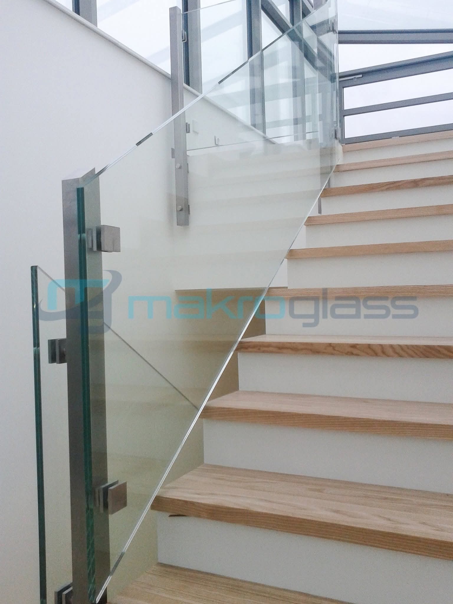 Szklana balustrada schodowa z metalowymi słupkami, widok z dołu. Nowoczesne rozwiązanie architektoniczne, jasne schody drewniane.